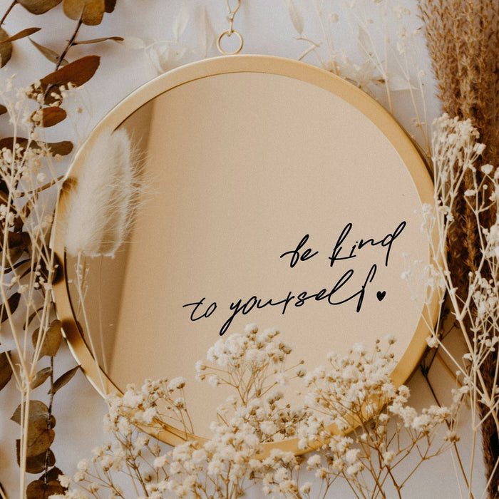 Black “Be Kind To Yourself” vinyl sticker on a round mirror with dried flowers