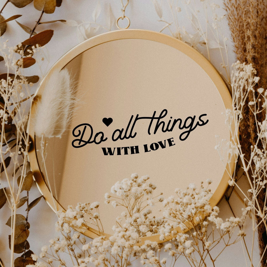 Black “Do All Things With Love” vinyl sticker on a round mirror with dried flowers