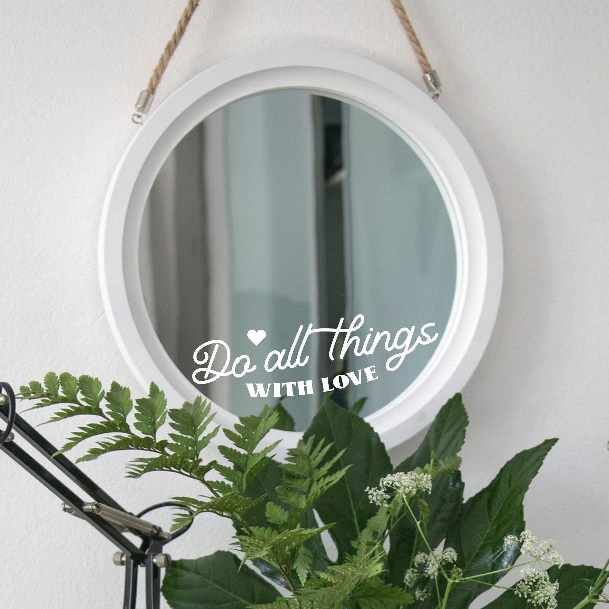 White “Do All Things With Love” mirror decal on a round white-framed mirror with green plants