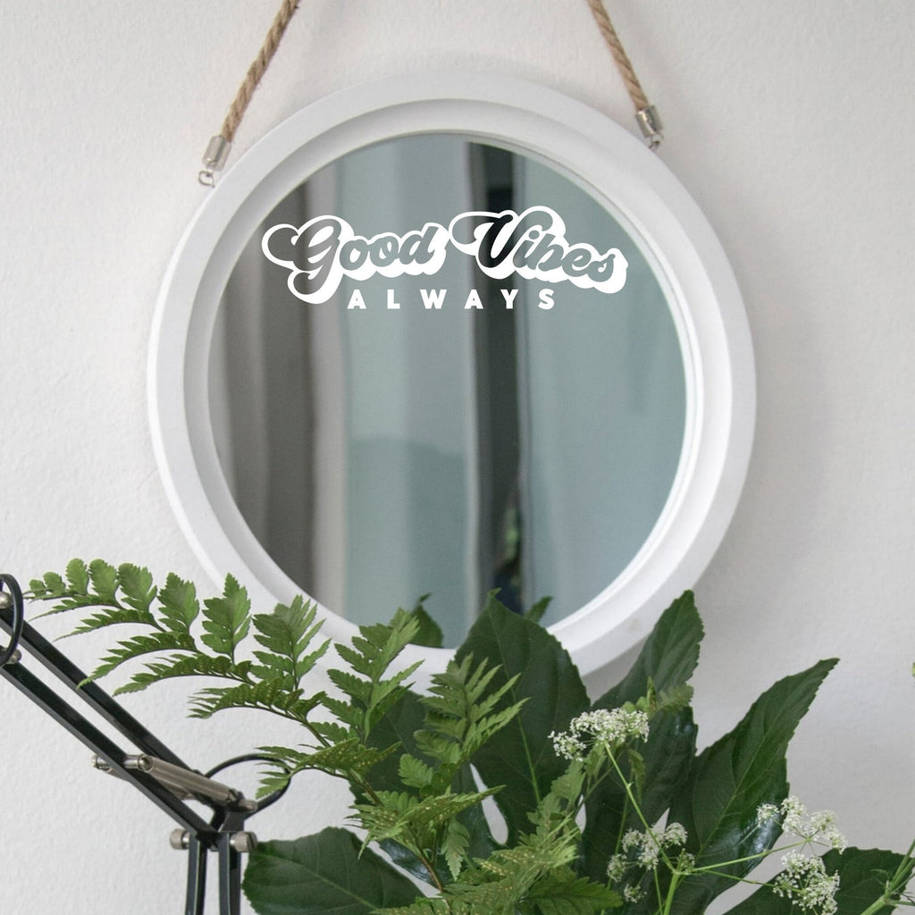 White “Good Vibes Always” mirror decal on a round white-framed mirror with green plants