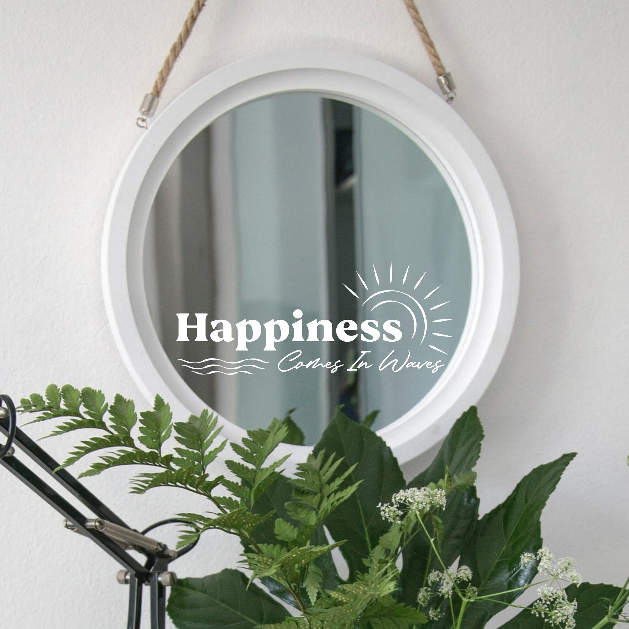 White “Happiness Comes In Waves” mirror decal on a round white-framed mirror with green plants