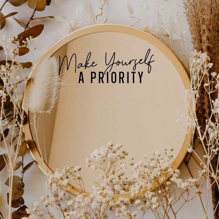 Black “Make Yourself A Priority” vinyl sticker on a round mirror with dried flowers