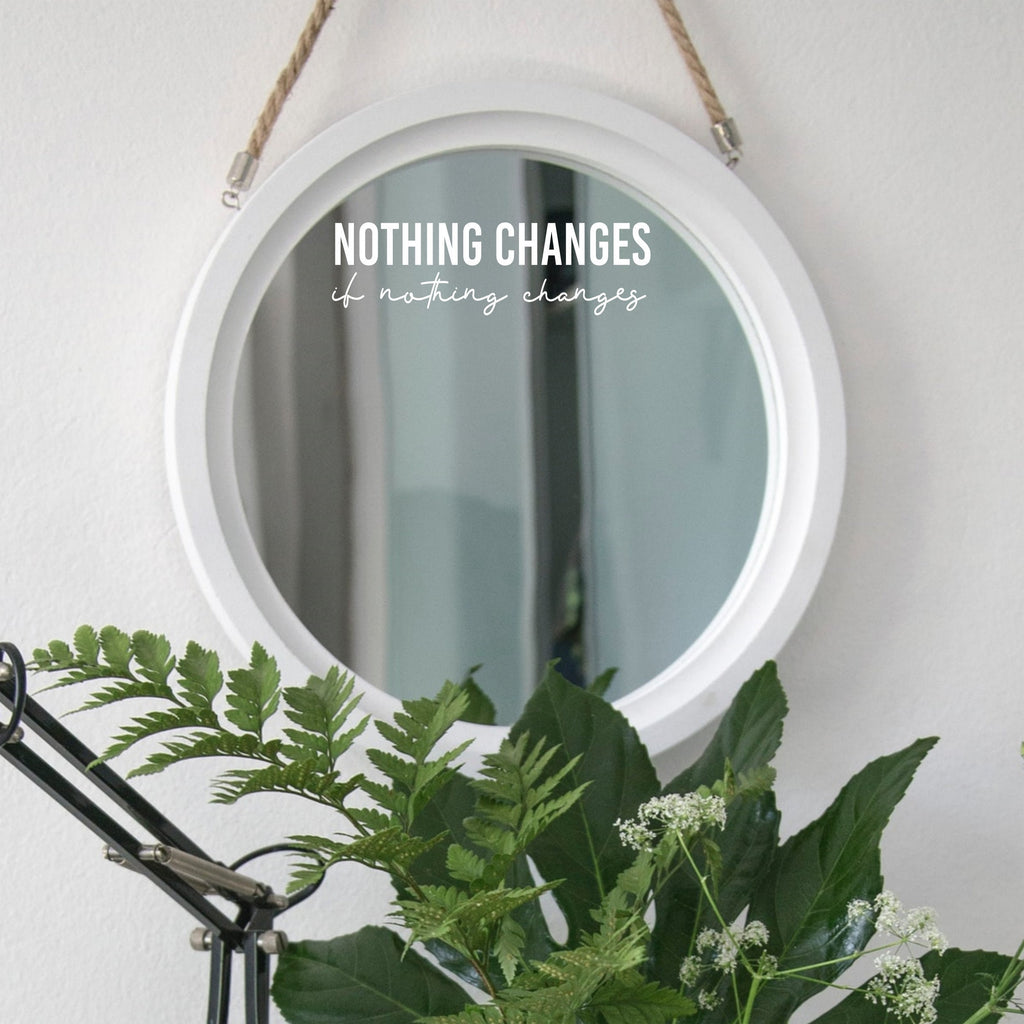 White “Nothing Changes If Nothing Changes” mirror decal on a round white-framed mirror with green plants