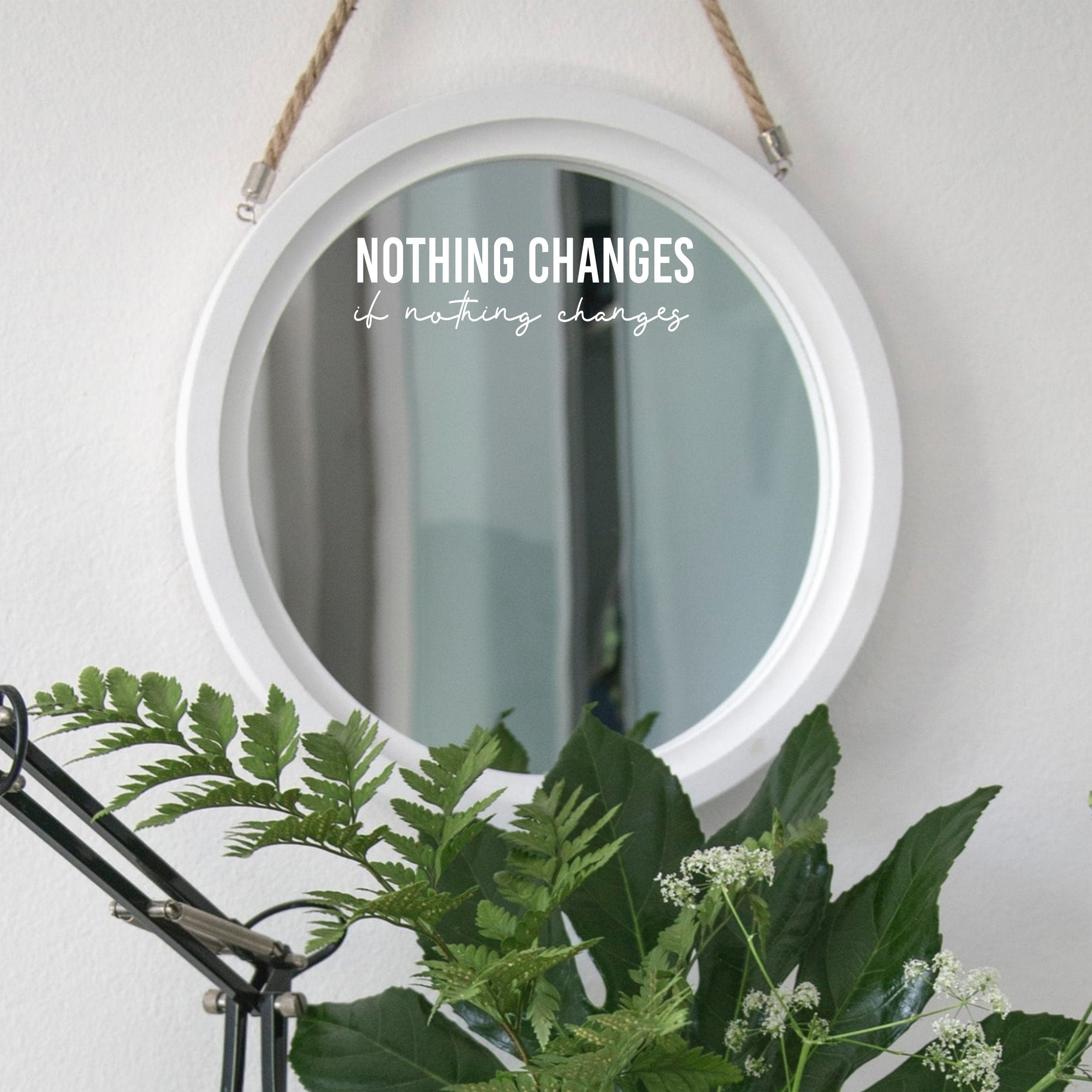 White “Nothing Changes If Nothing Changes” mirror decal on a round white-framed mirror with green plants