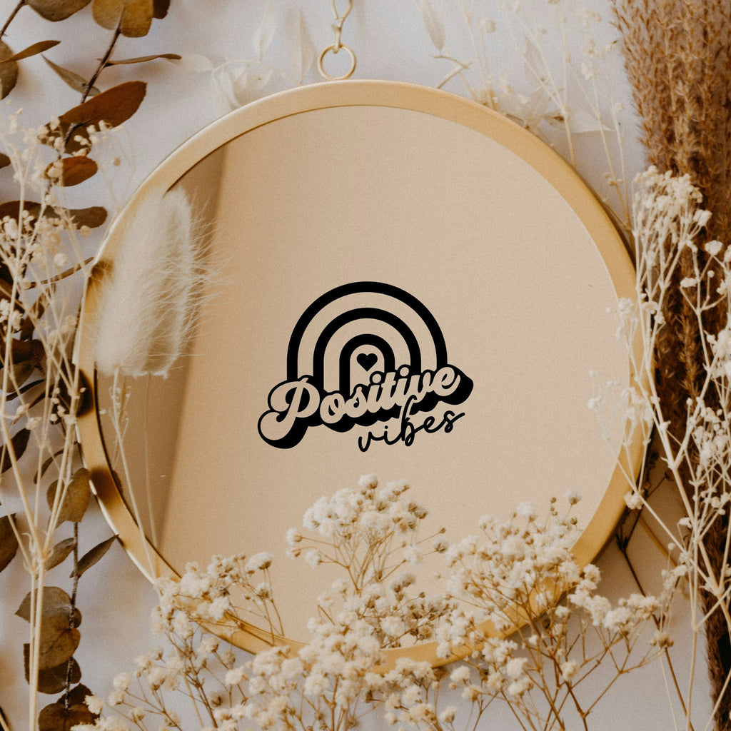 Black “Positive Vibes” vinyl sticker on a round mirror with dried flowers