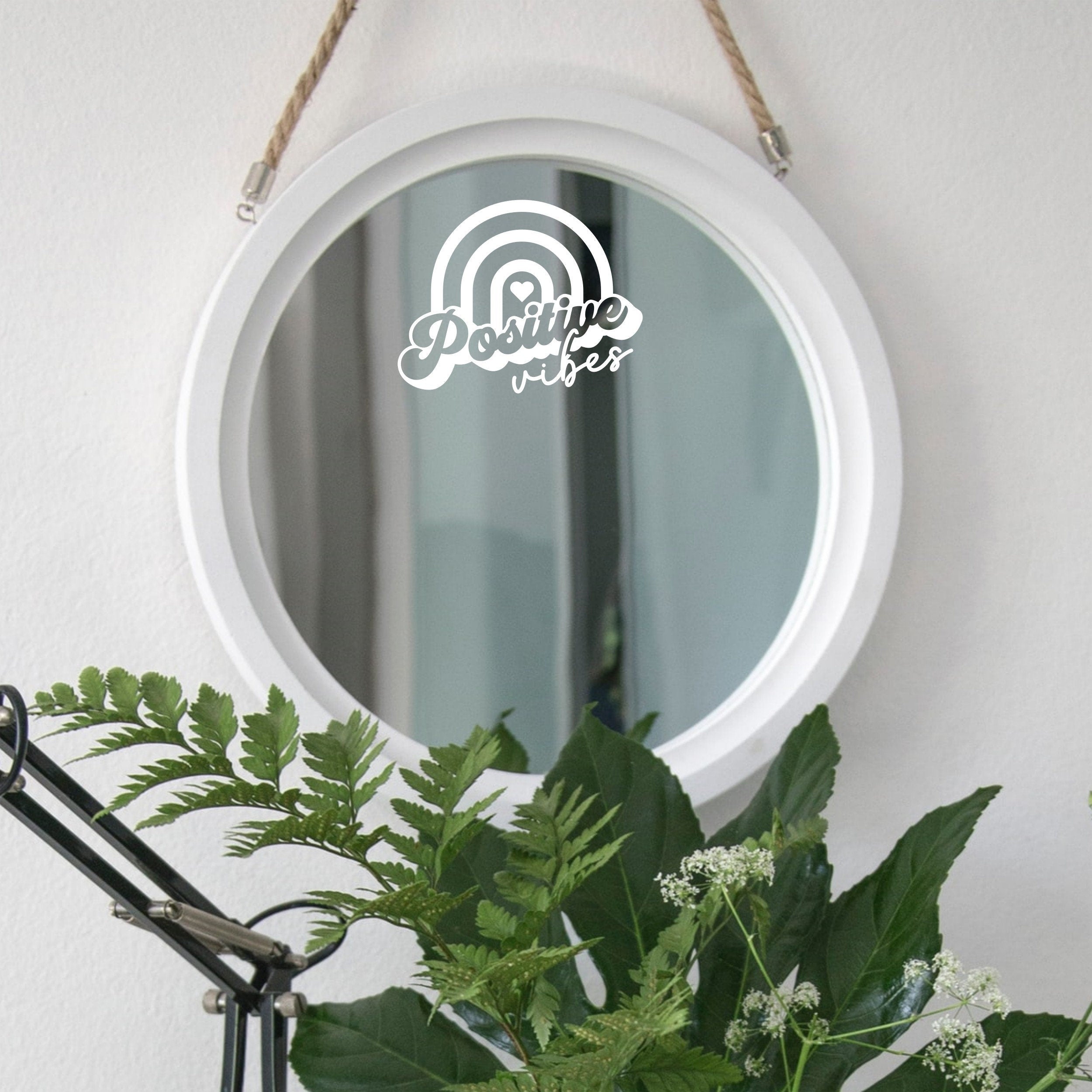 White “Positive Vibes” mirror decal on a round white-framed mirror with green plants