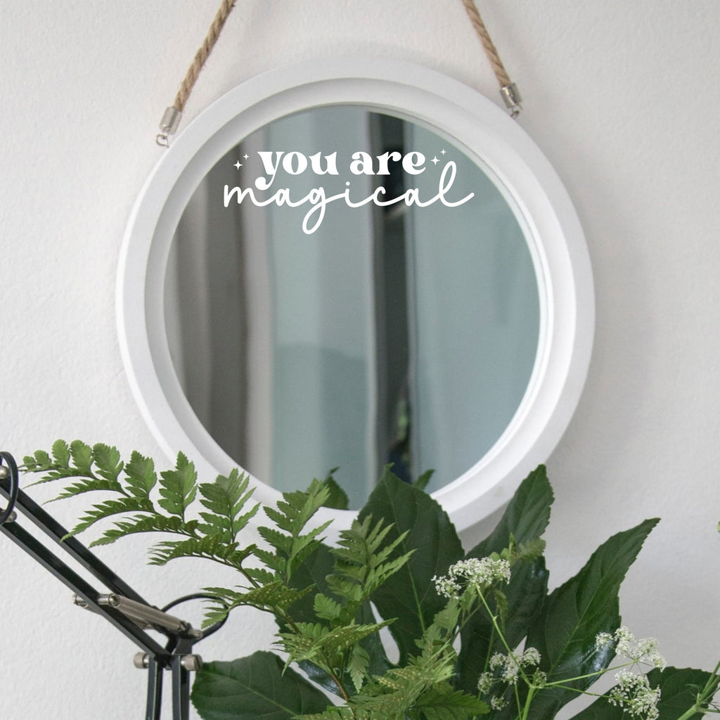 White “You Are Magical” mirror decal on a round white-framed mirror with green plants
