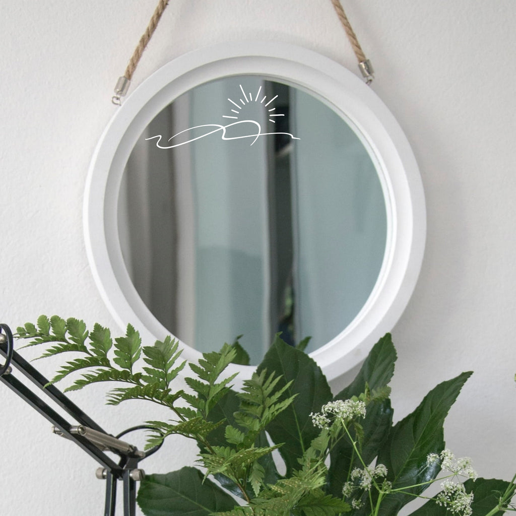 White “Sunrise” mirror decal on a round white-framed mirror with green plants