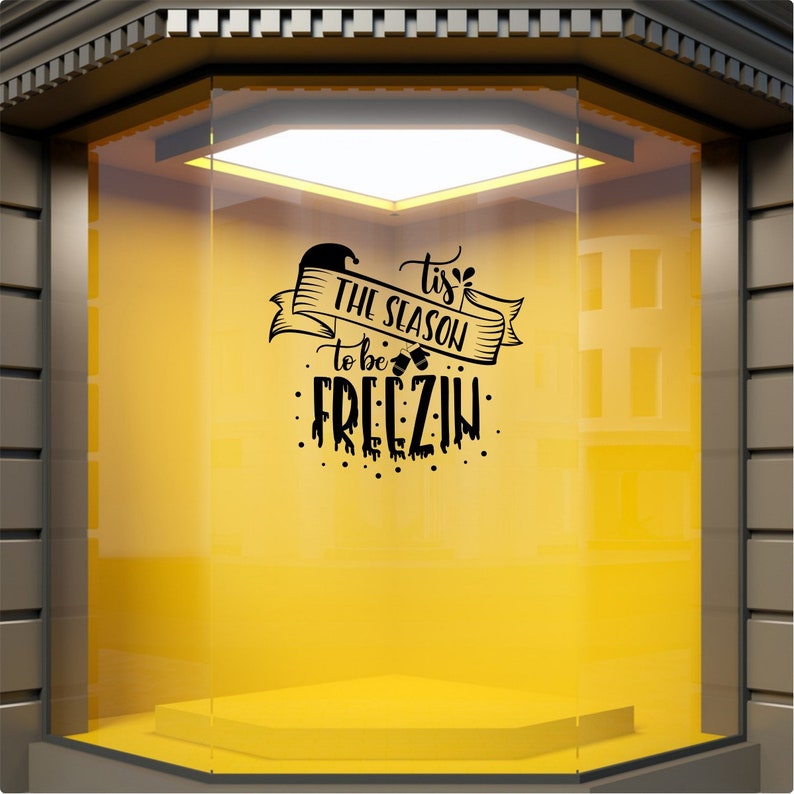 Black Tis the Season to Be Freezin Christmas sticker on a yellow shopfront