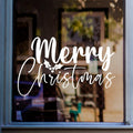 White Merry Christmas script vinyl decal displayed on a glass window, showing the decorative festive lettering applied to glass.