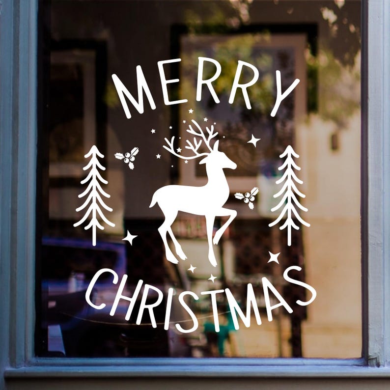 Merry Christmas white vinyl window sticker featuring a reindeer, fir trees, stars and snowflakes displayed on glass.
