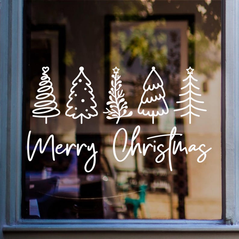 White Merry Christmas window sticker featuring five decorative Christmas trees displayed on a glass window.