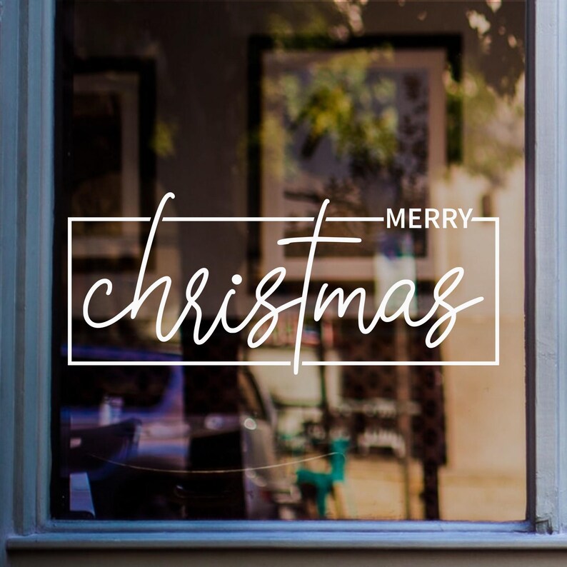 White Merry Christmas window sticker with modern handwritten lettering and a minimal rectangular border displayed on glass.
