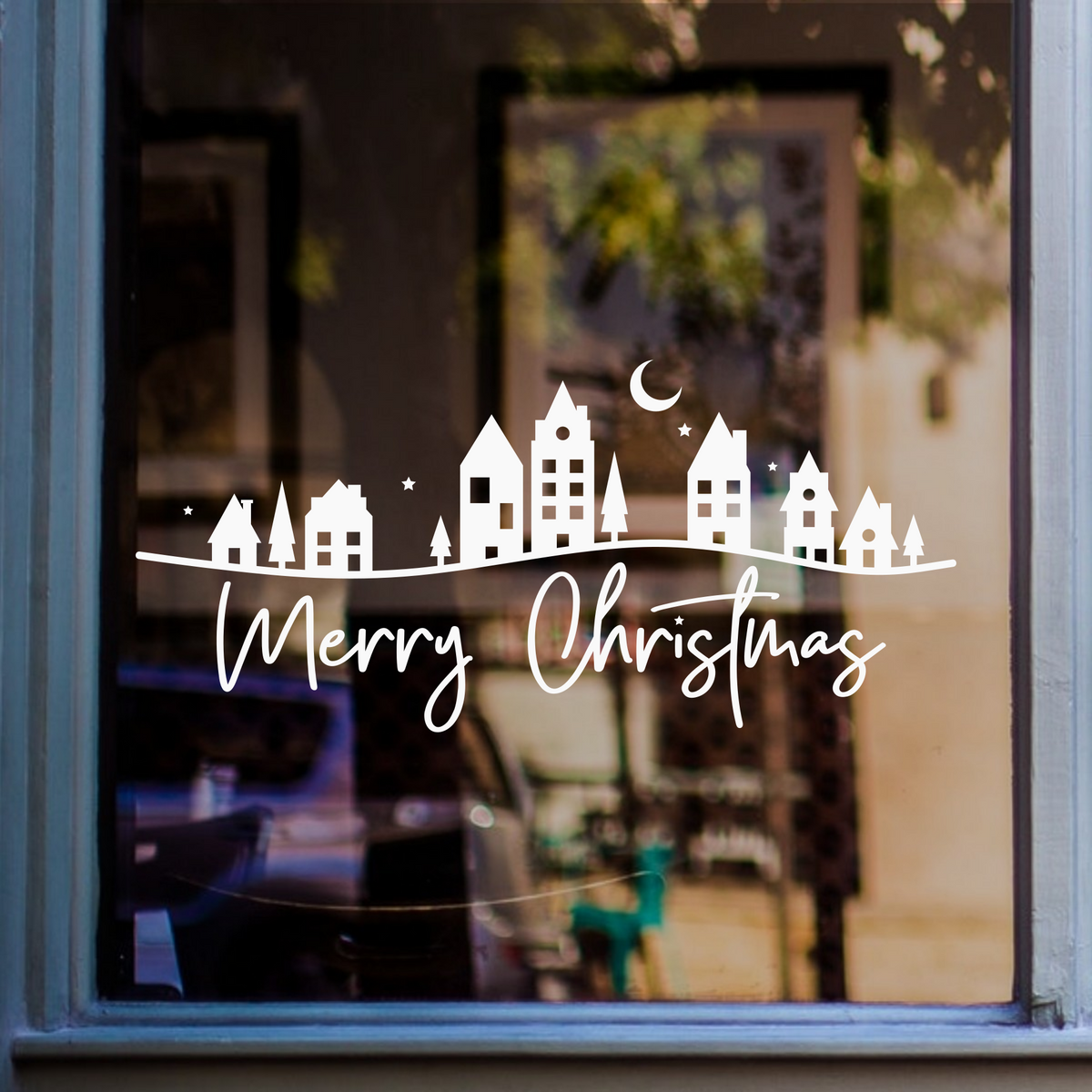White Merry Christmas village window sticker with houses, trees, stars and crescent moon displayed on a shop window