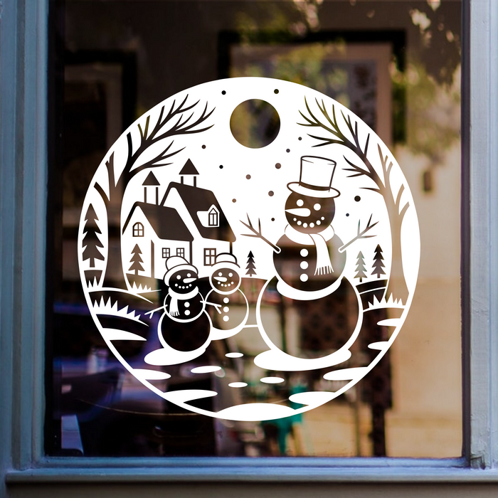 Christmas snowman village window sticker featuring three snowmen, houses, fir trees and snowy branches in a circular winter scene.