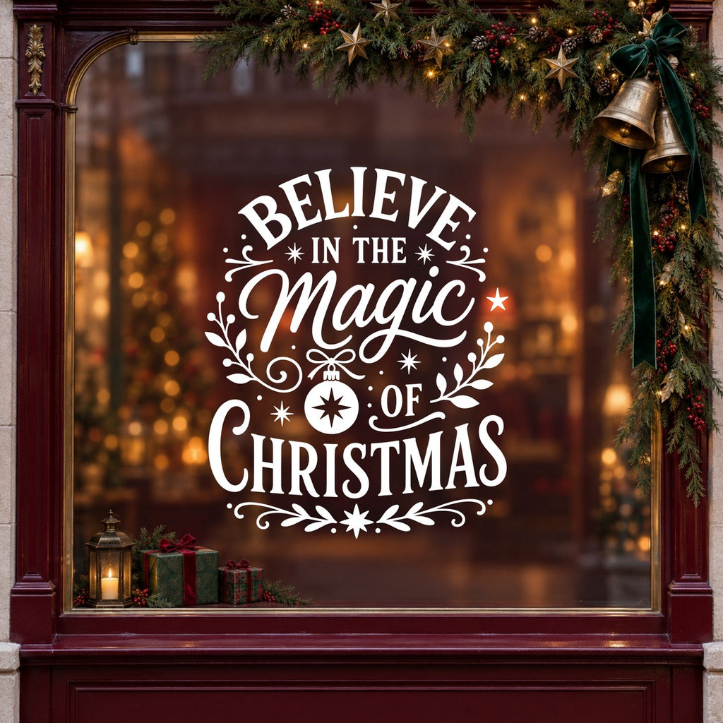 Believe in the Magic of Christmas Window Sticker in white on a burgundy shop window with festive greenery, bells and gifts