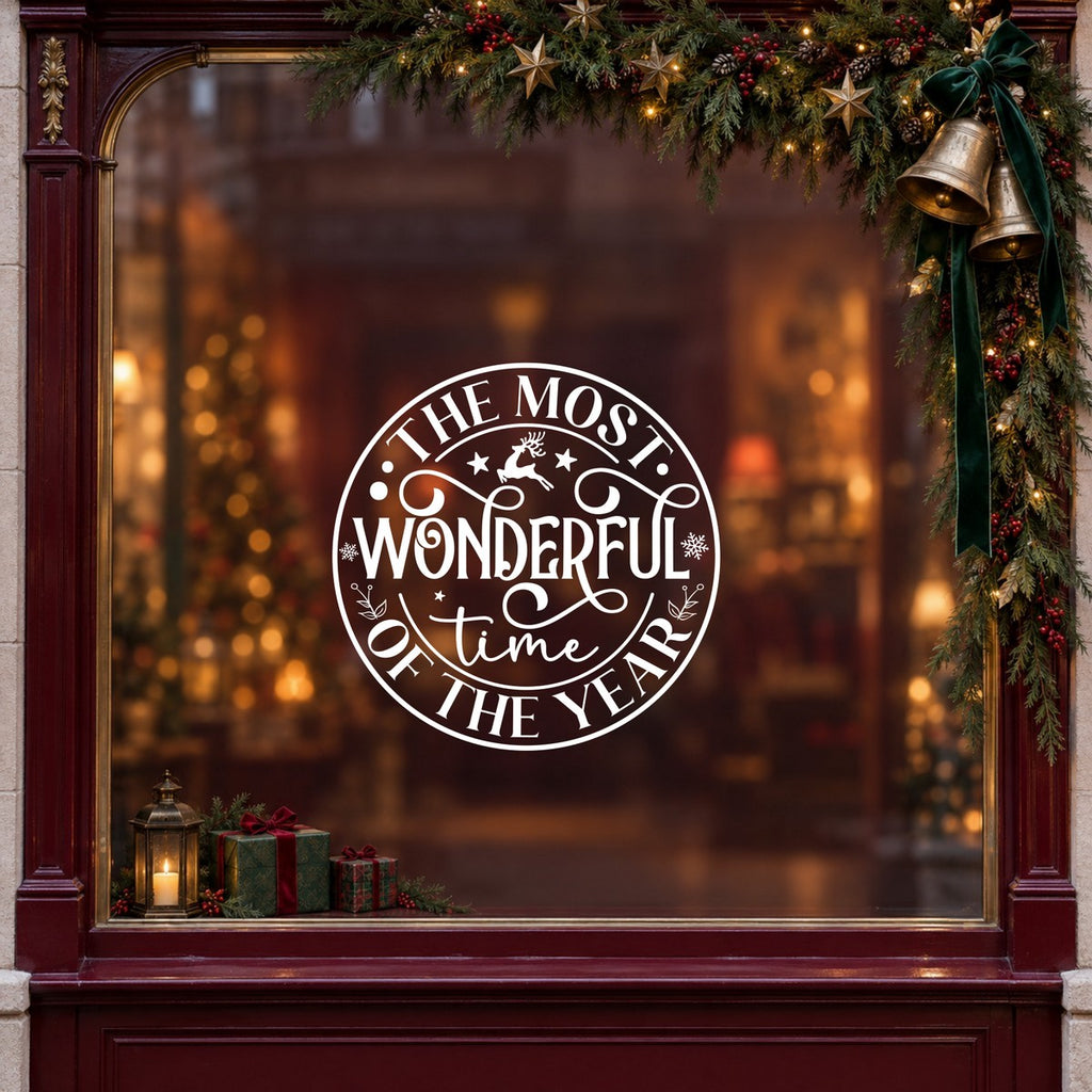 Round Most Wonderful Time of the Year Window Sticker in white on a burgundy shop window with festive greenery, bells and gifts