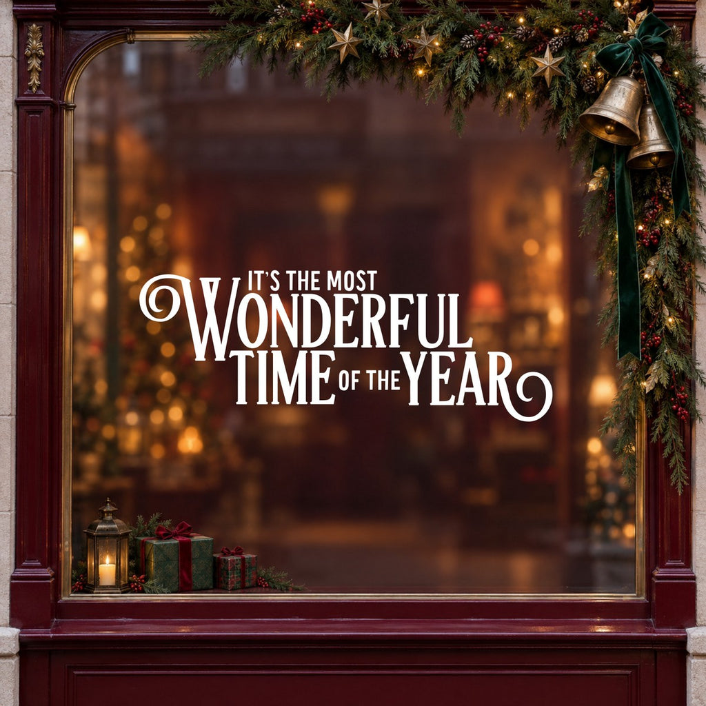 Most Wonderful Time of the Year Christmas Window Sticker in white on a burgundy shop window with festive greenery, bells and gifts