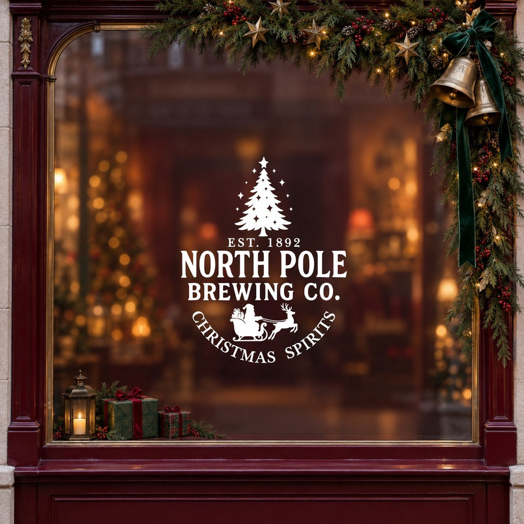 North Pole Brewing Co Christmas Window Sticker in white on a burgundy shop window with festive greenery, bells and gifts
