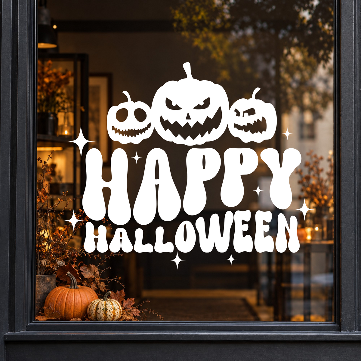 Pumpkins Happy Halloween window sticker showing three jack-o’-lantern pumpkins above bold Happy Halloween lettering, white vinyl on a dark shop window with a charcoal frame