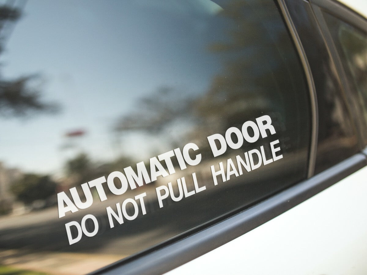 White Automatic Door Do Not Pull Handle sticker on a vehicle window.