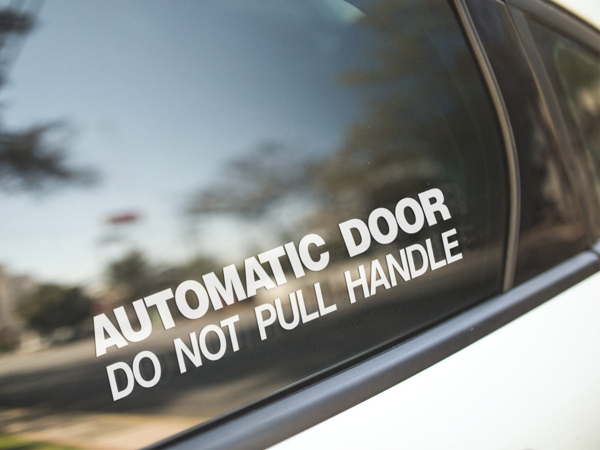 White Automatic Door Do Not Pull Handle sticker on a vehicle window.