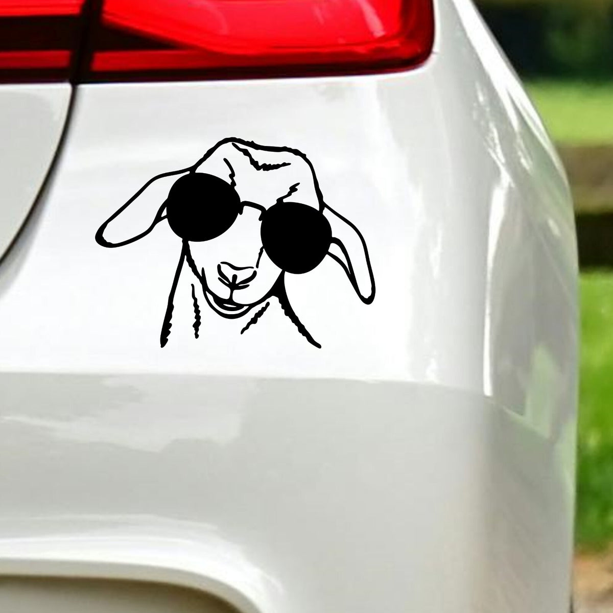 Black goat with sunglasses sticker on white car bodywork beneath a rear light.