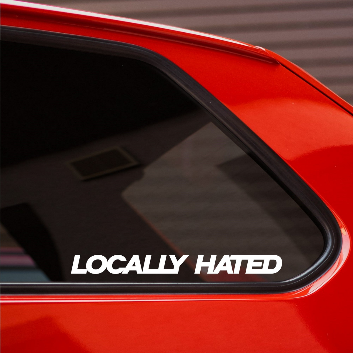 White Locally Hated bold italic decal on the rear side window of a red car.