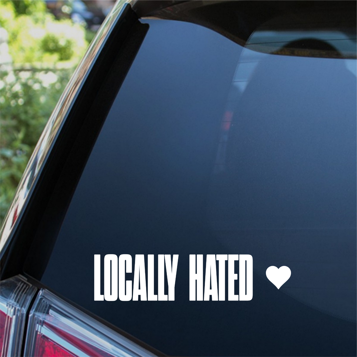 White Locally Hated lettering and heart decal on a car rear window.
