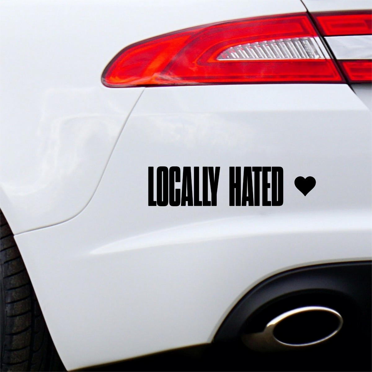Black Locally Hated lettering and heart decal on a white car rear bumper.