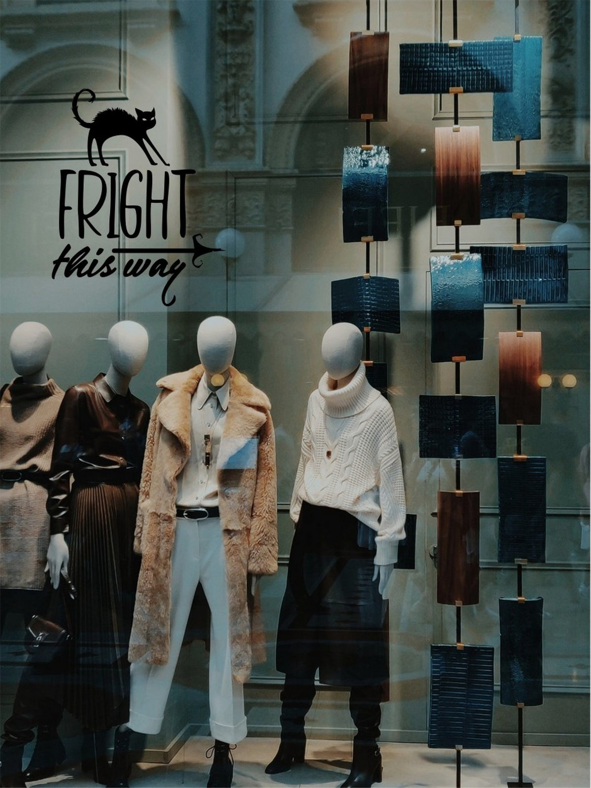Black Fright This Way Halloween window sticker above mannequins in a clothing shop display.