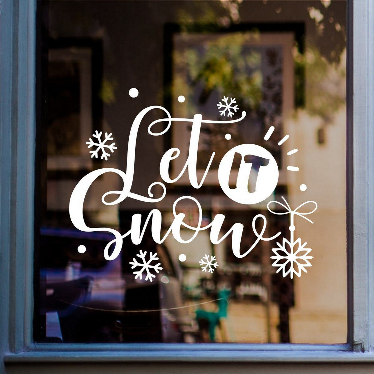 White Let It Snow lettering, snowflakes and hanging ornament on a blue-grey framed window.