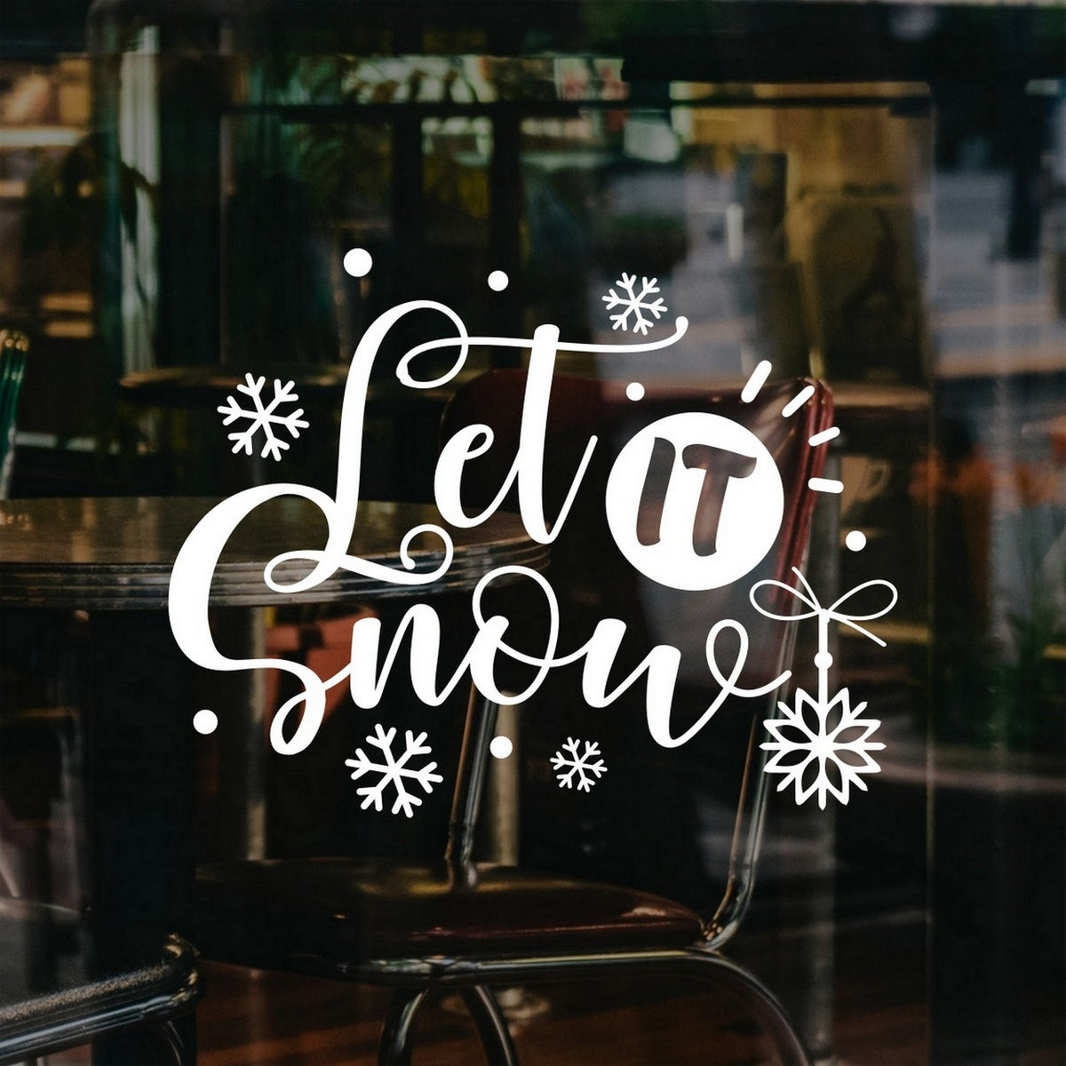 White Let It Snow script window sticker with snowflakes and a hanging ornament on a cafe window.