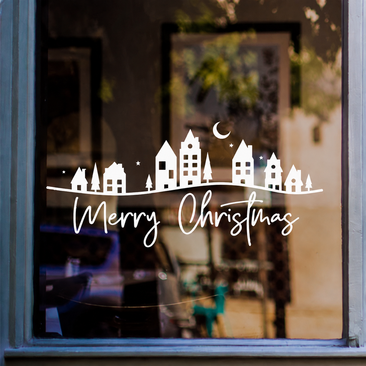 White Merry Christmas village window sticker with houses, trees, stars and crescent moon displayed on a shop window
