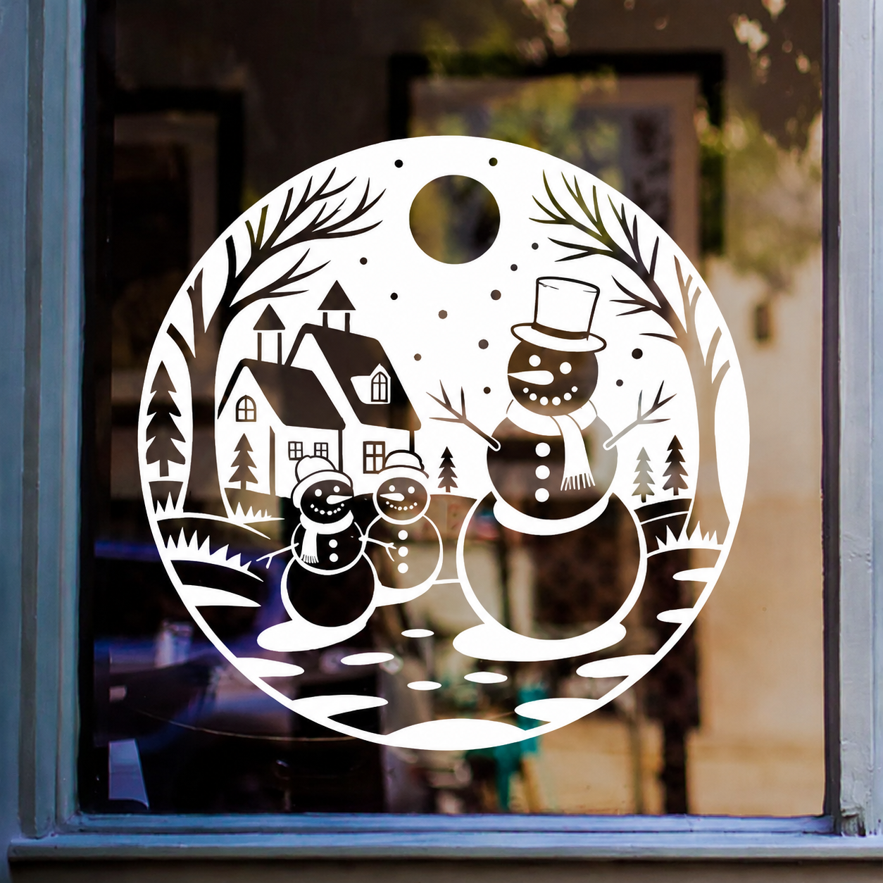 Christmas snowman village window sticker featuring three snowmen, houses, fir trees and snowy branches in a circular winter scene.
