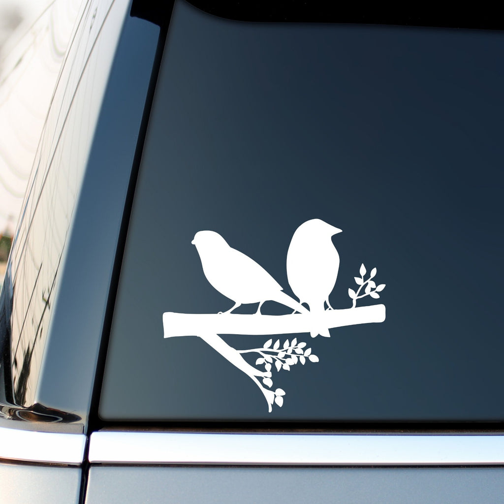 White two birds on a branch sticker on a vehicle side window.