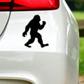 Black walking bigfoot sticker on white car bodywork beneath a rear light.