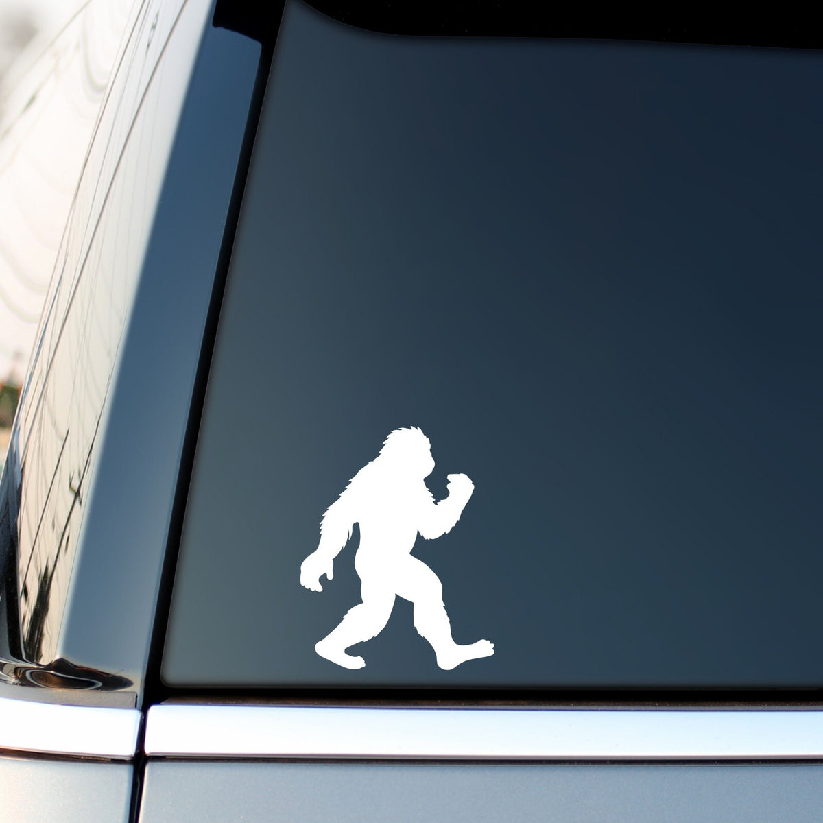 White walking bigfoot sticker on a vehicle side window.